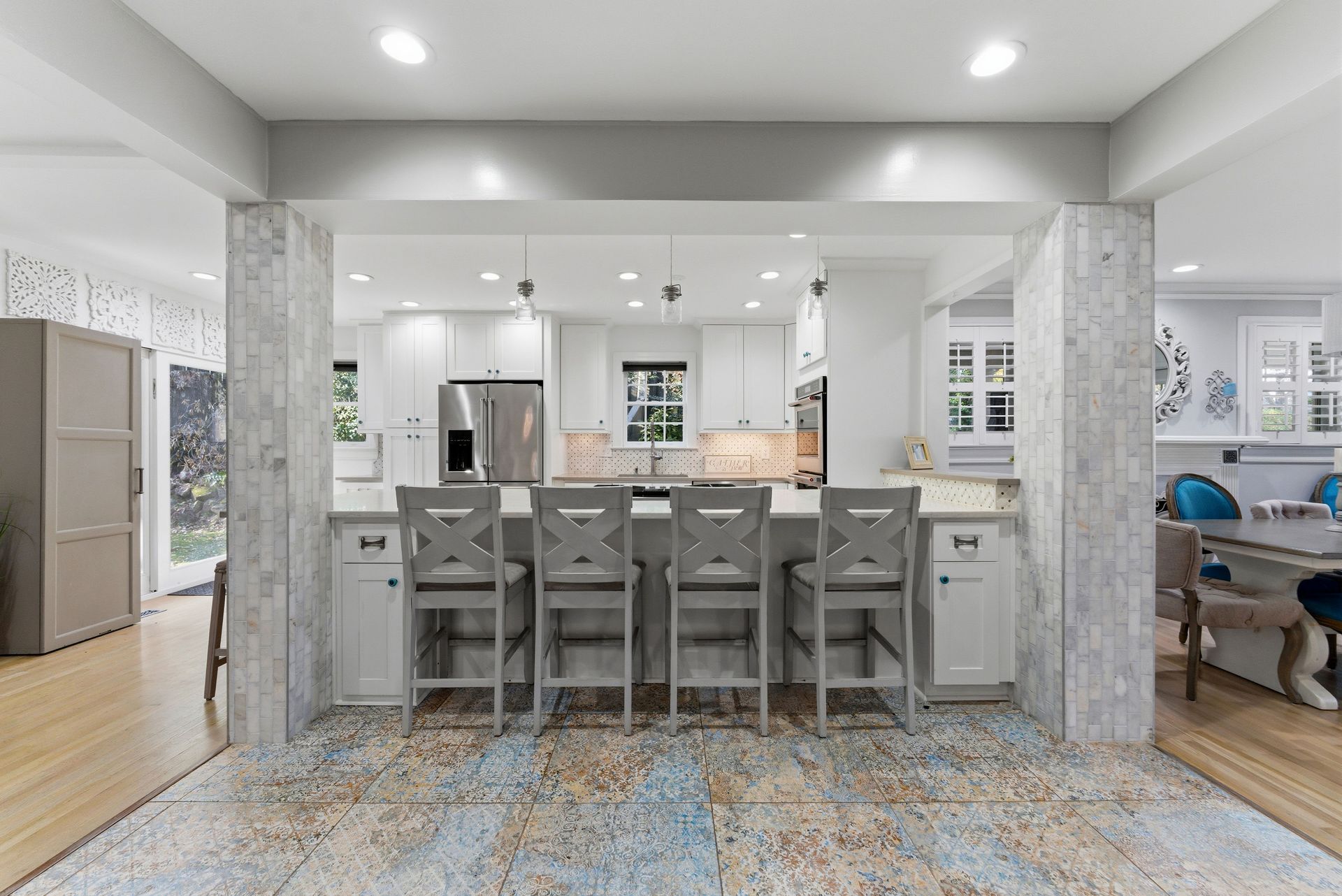 A bright, open-plan kitchen with a white island, four gray bar stools, and stone-tiled support columns.