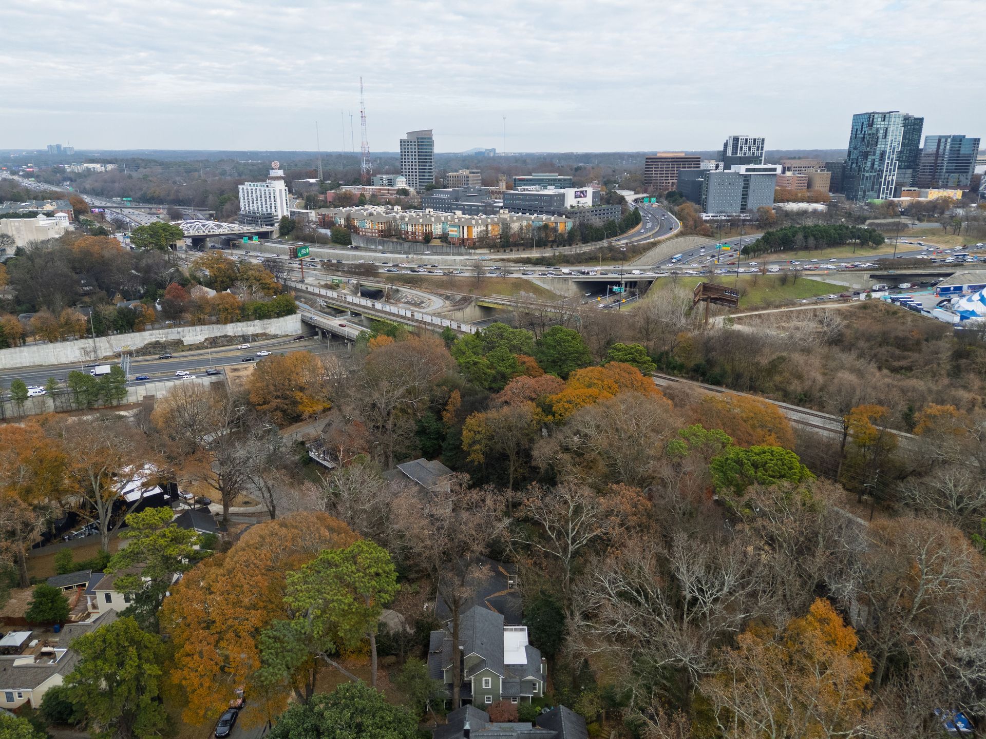 Aerial view of a residential neighborhood with autumn trees nestled beside a busy highway and city skyline in the distance.