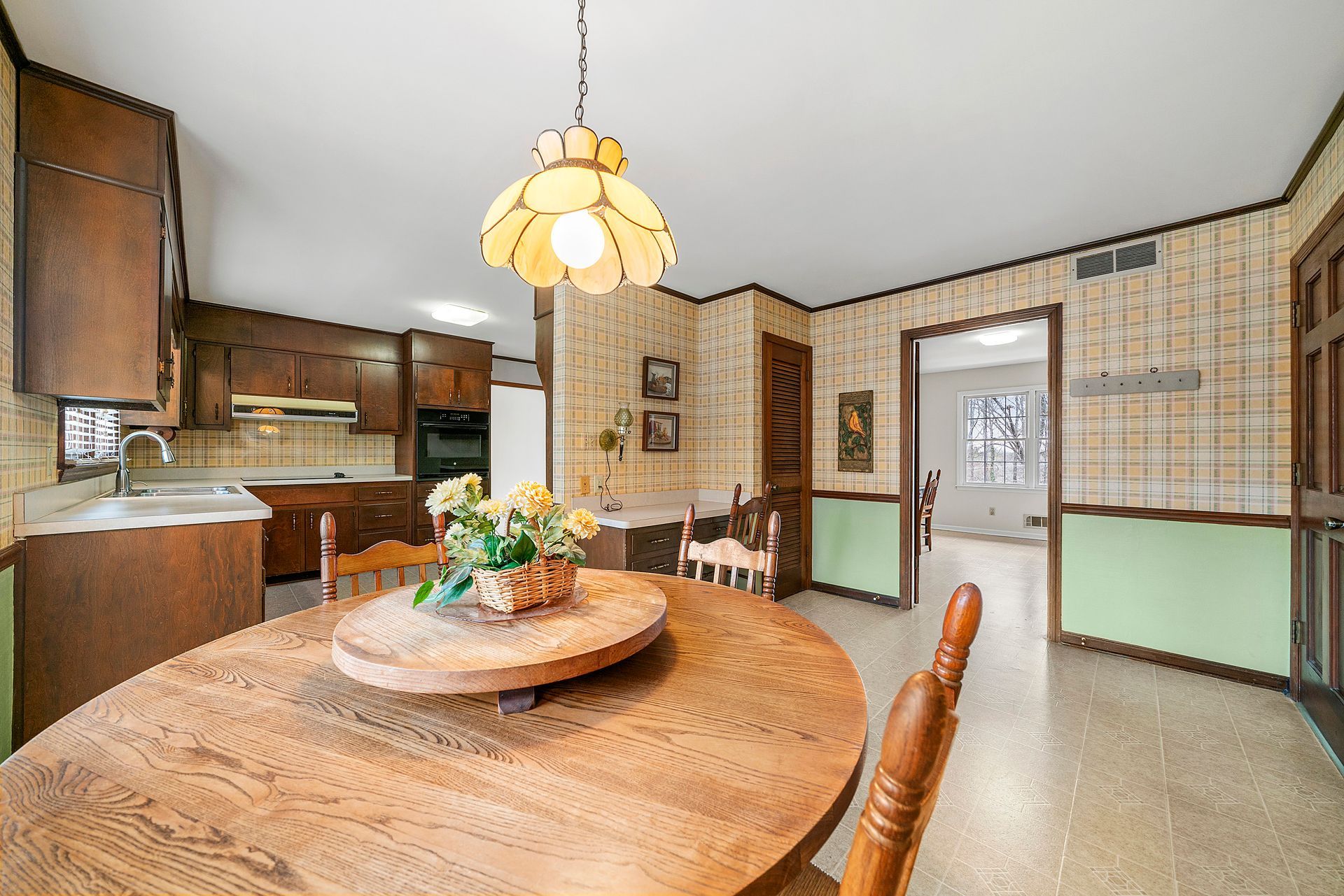 A kitchen with a wooden table and chairs and a stained glass light fixture.