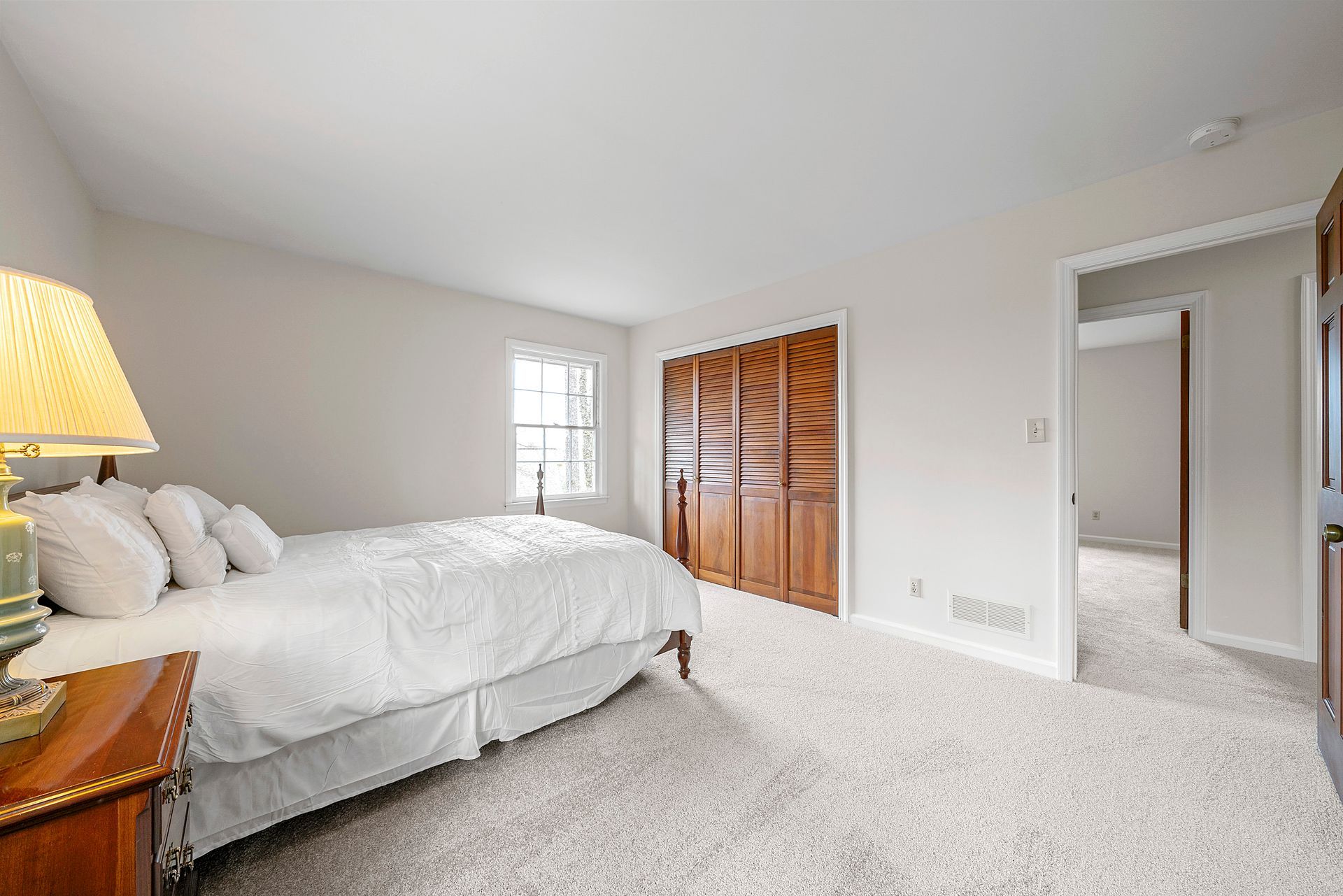 A bedroom with a bed , nightstand , lamp and closet.
