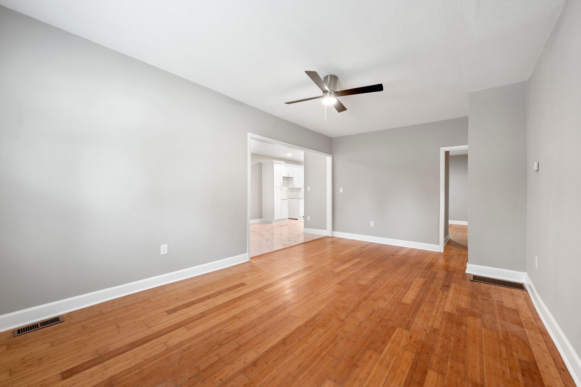 Empty room with hardwood floors, gray walls, ceiling fan, doorway to another space.