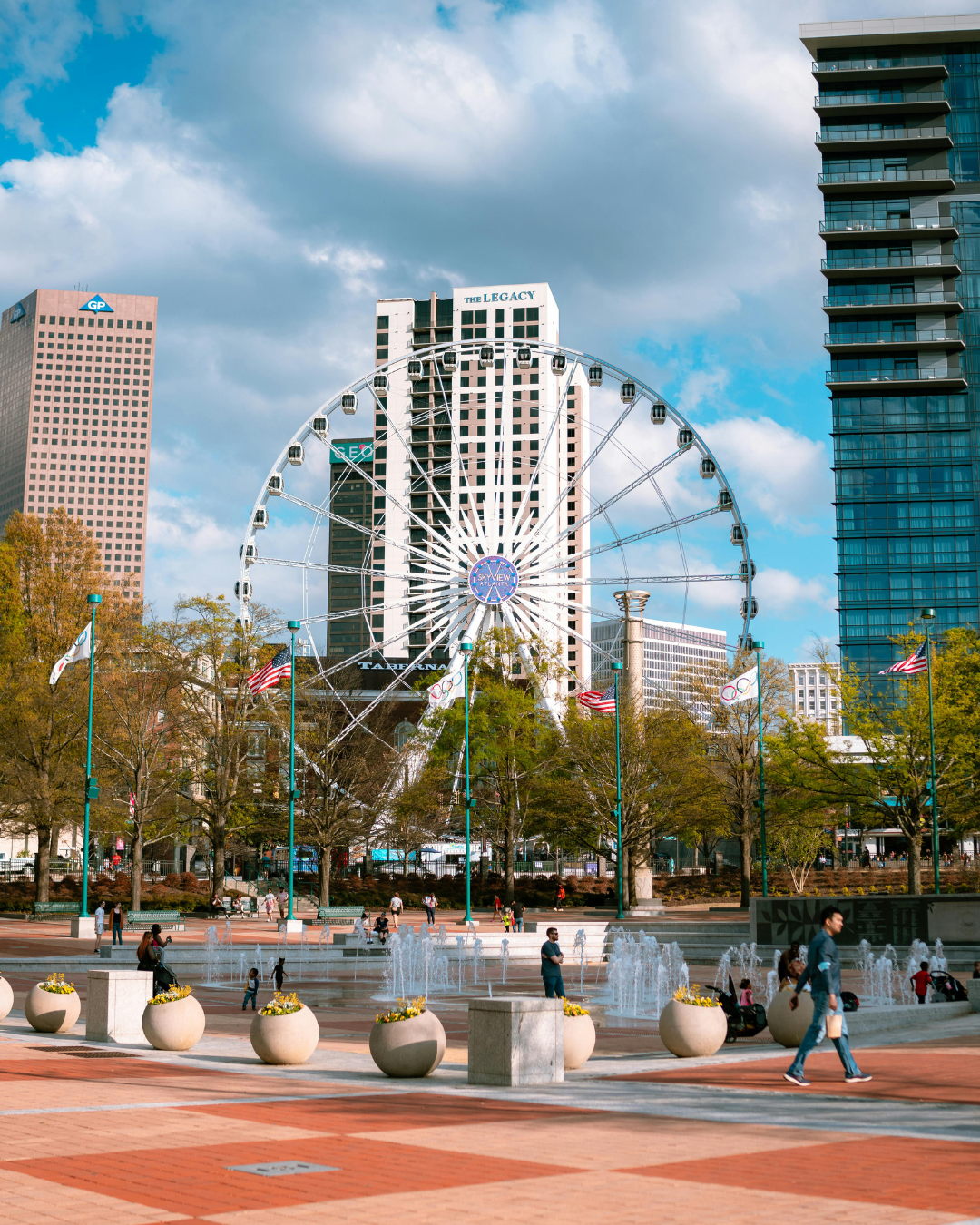 Ferris wheel in city park, with fountains, buildings, and blue sky.
