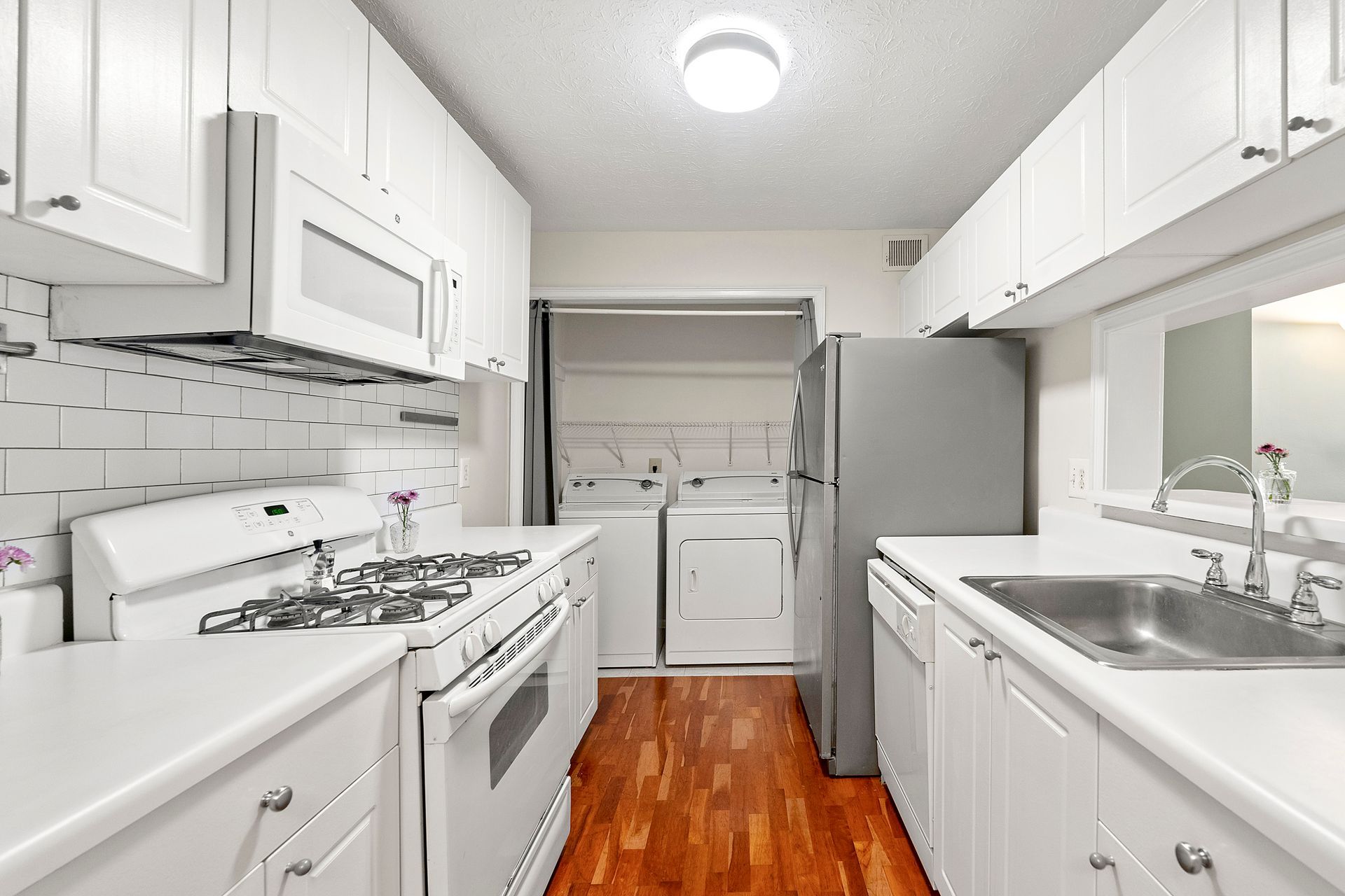 A kitchen with white cabinets , a stove , a refrigerator , and a sink.