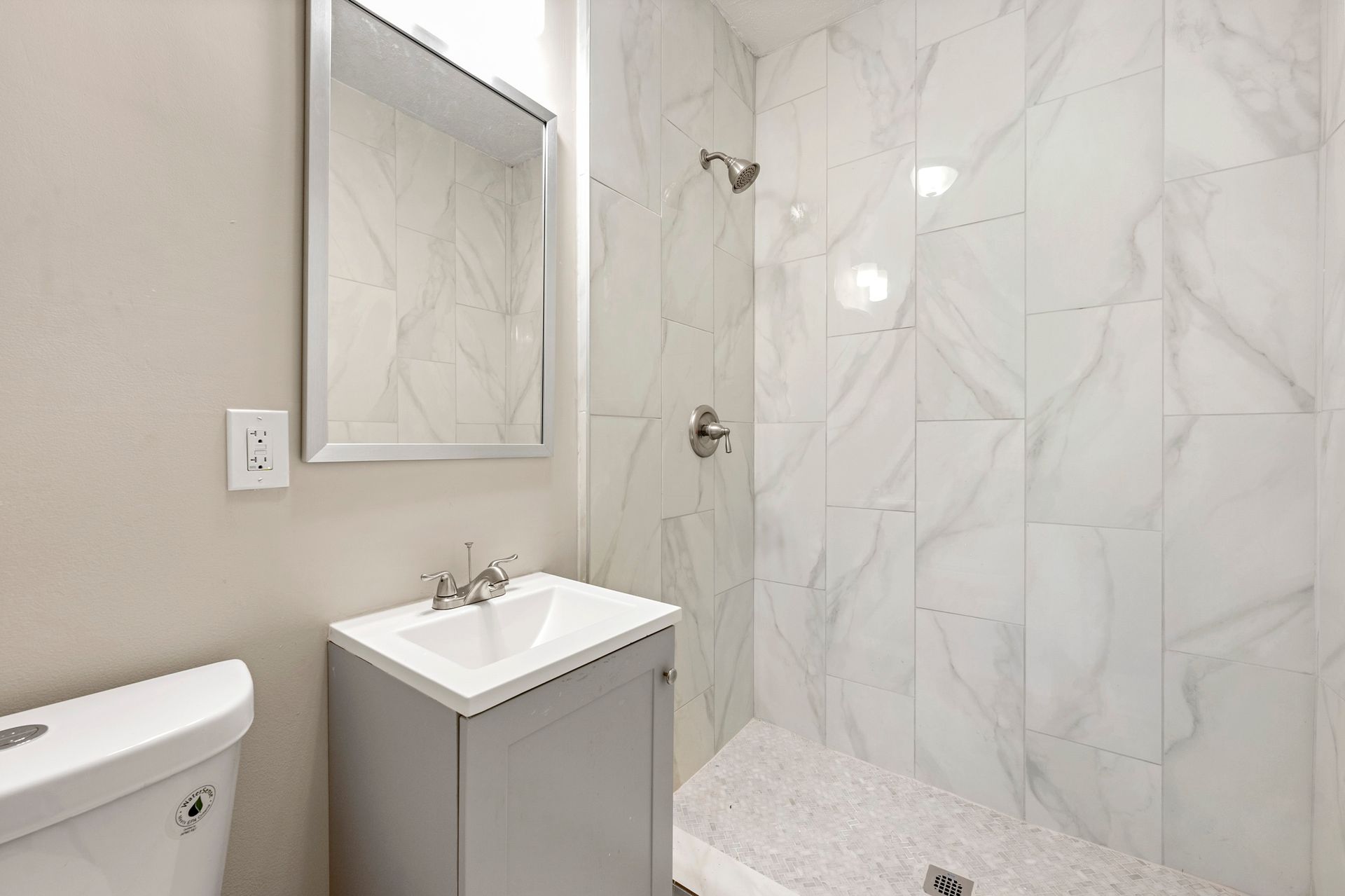 Bathroom with gray vanity, white toilet, and marble tile shower.