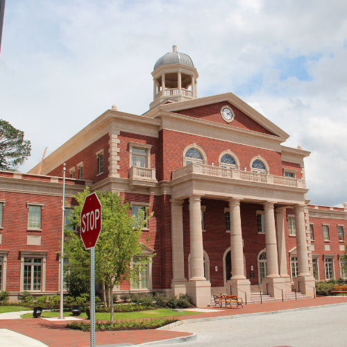 A red-brick courthouse with a columned portico and cupola stands behind a stop sign on a sunny day.