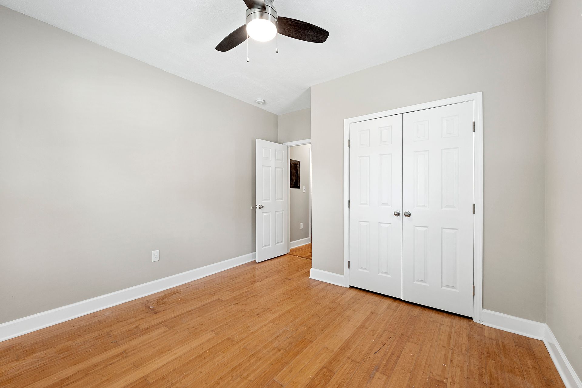Empty bedroom with light wood floor, white doors, and a ceiling fan.