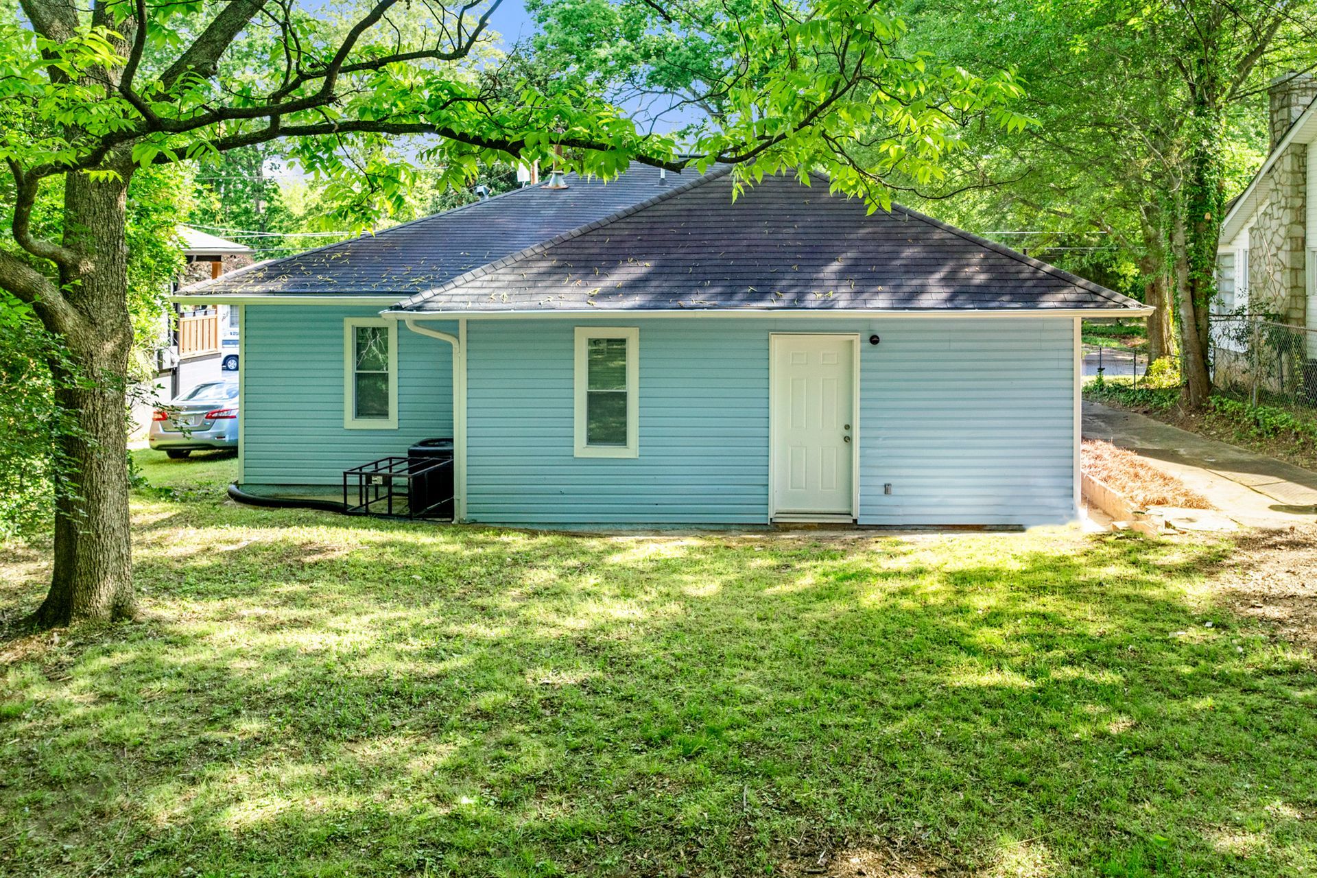 Light blue house with white trim, door, and windows, on a green lawn, under trees.