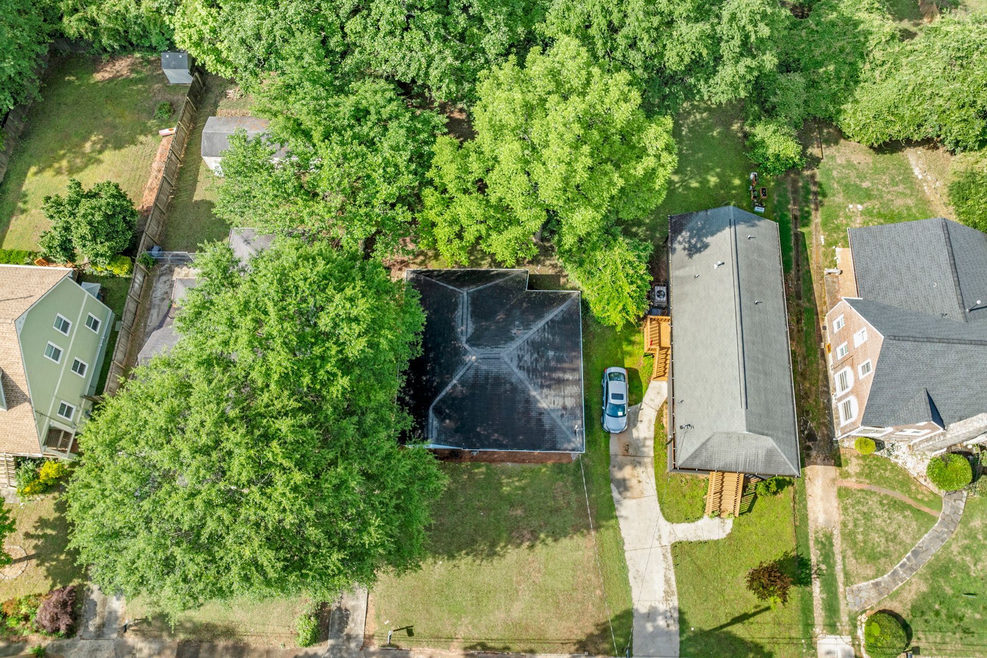 Overhead view of homes surrounded by trees, with a driveway and car visible.
