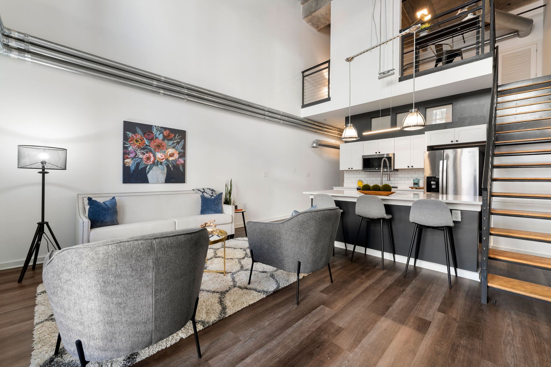 A living room with a couch , chairs , stairs and a kitchen.