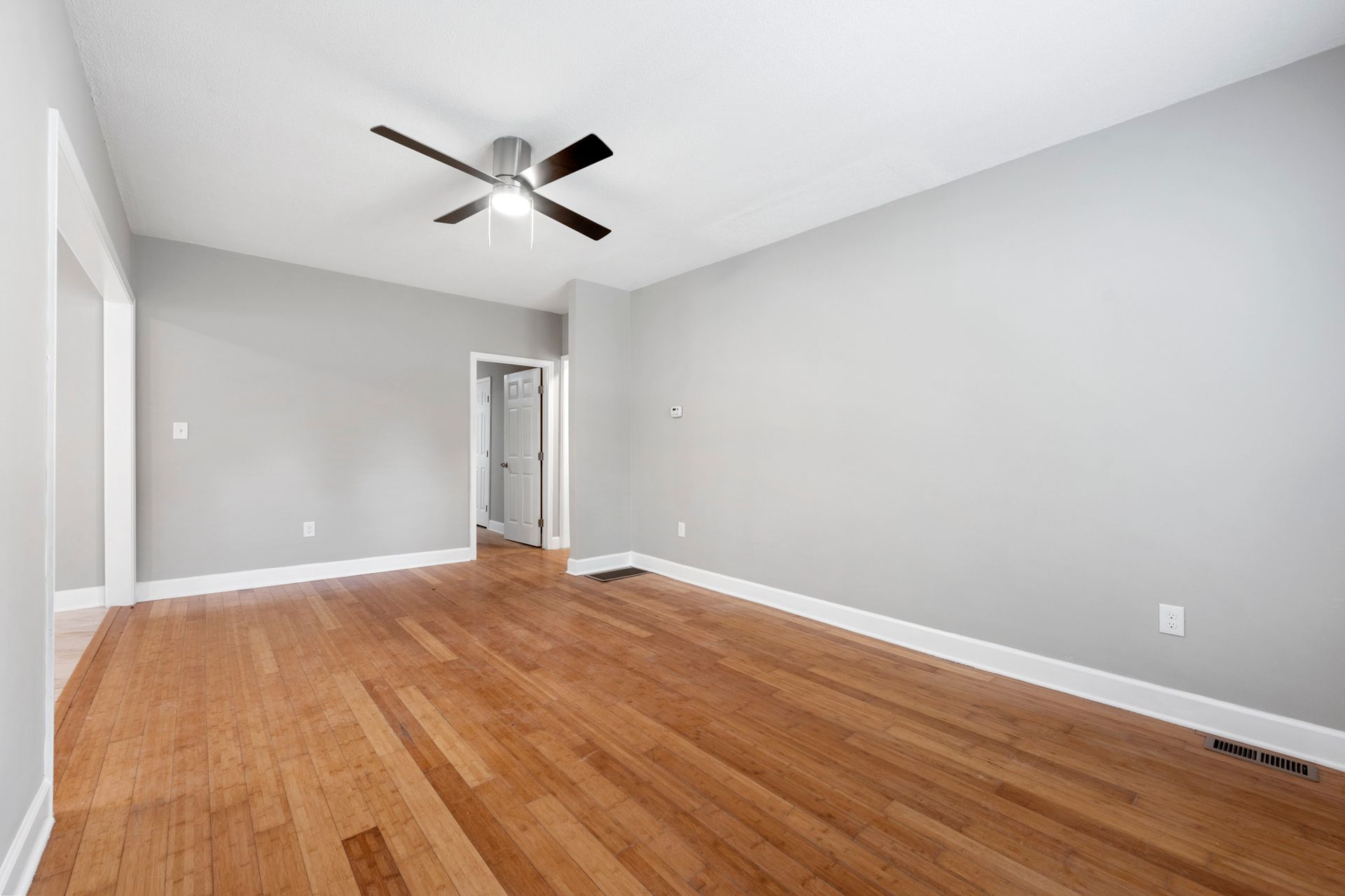 Empty room with hardwood floors, gray walls, ceiling fan, and doorway.