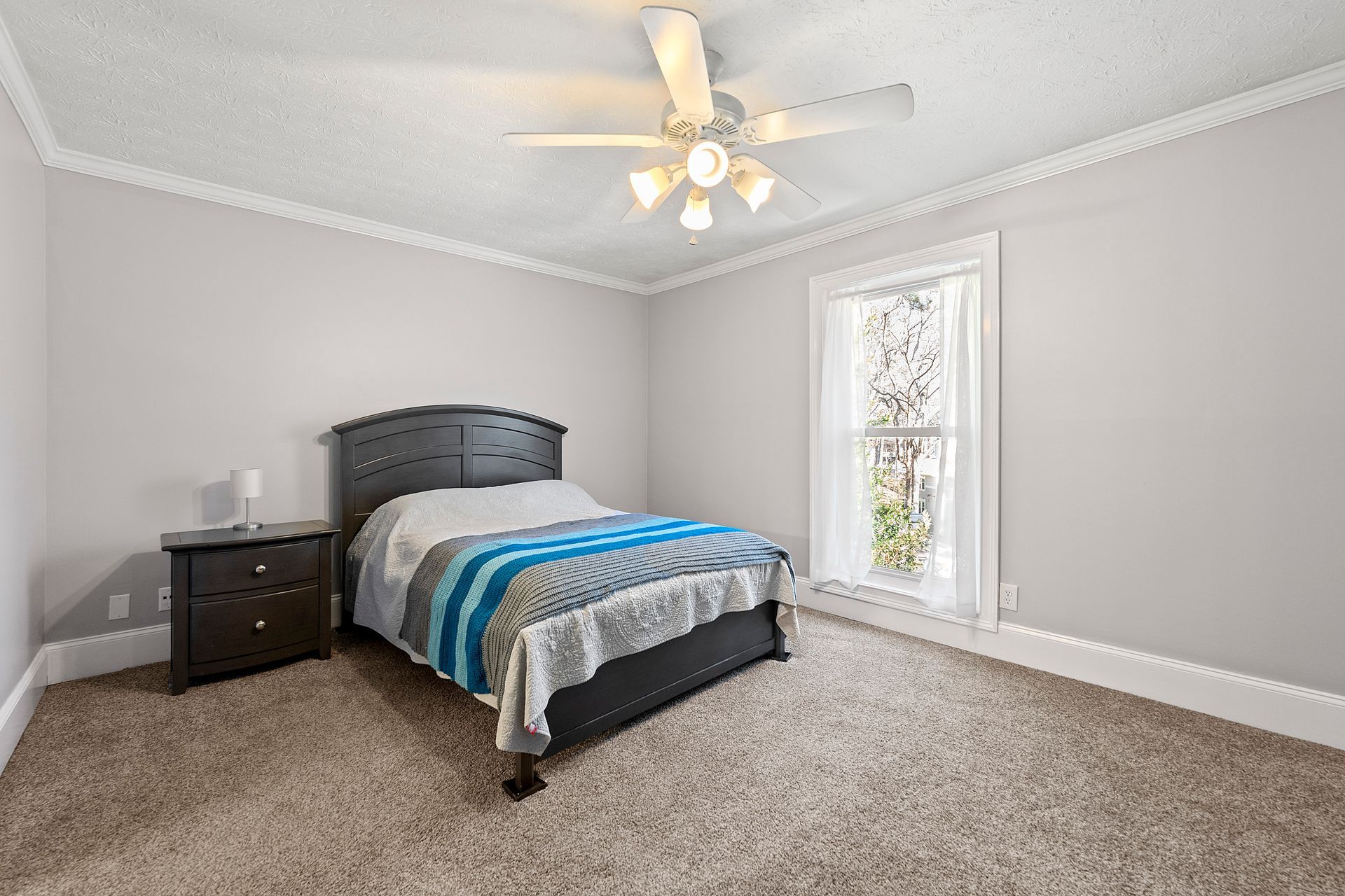 A bedroom with a bed , nightstand , ceiling fan and window.