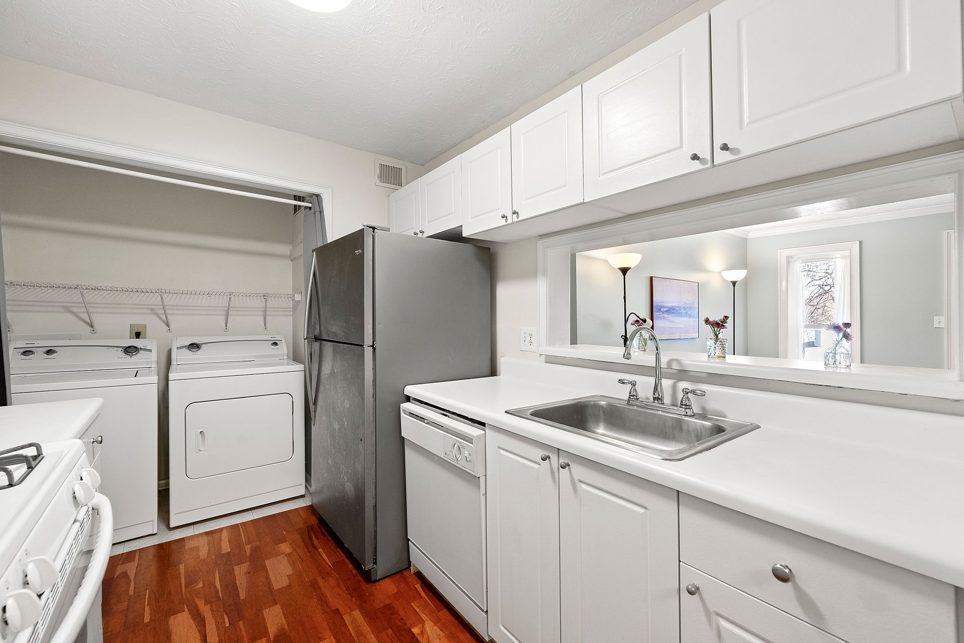 A kitchen with white cabinets , a refrigerator , a sink , and a washer and dryer.