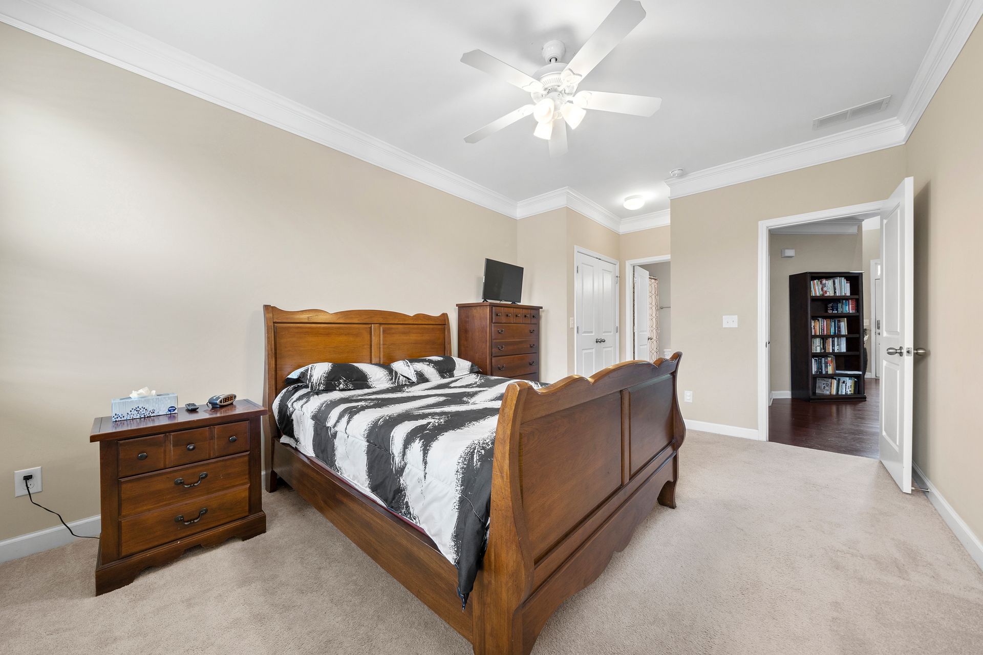 A bedroom with a bed , nightstand , dresser and ceiling fan.