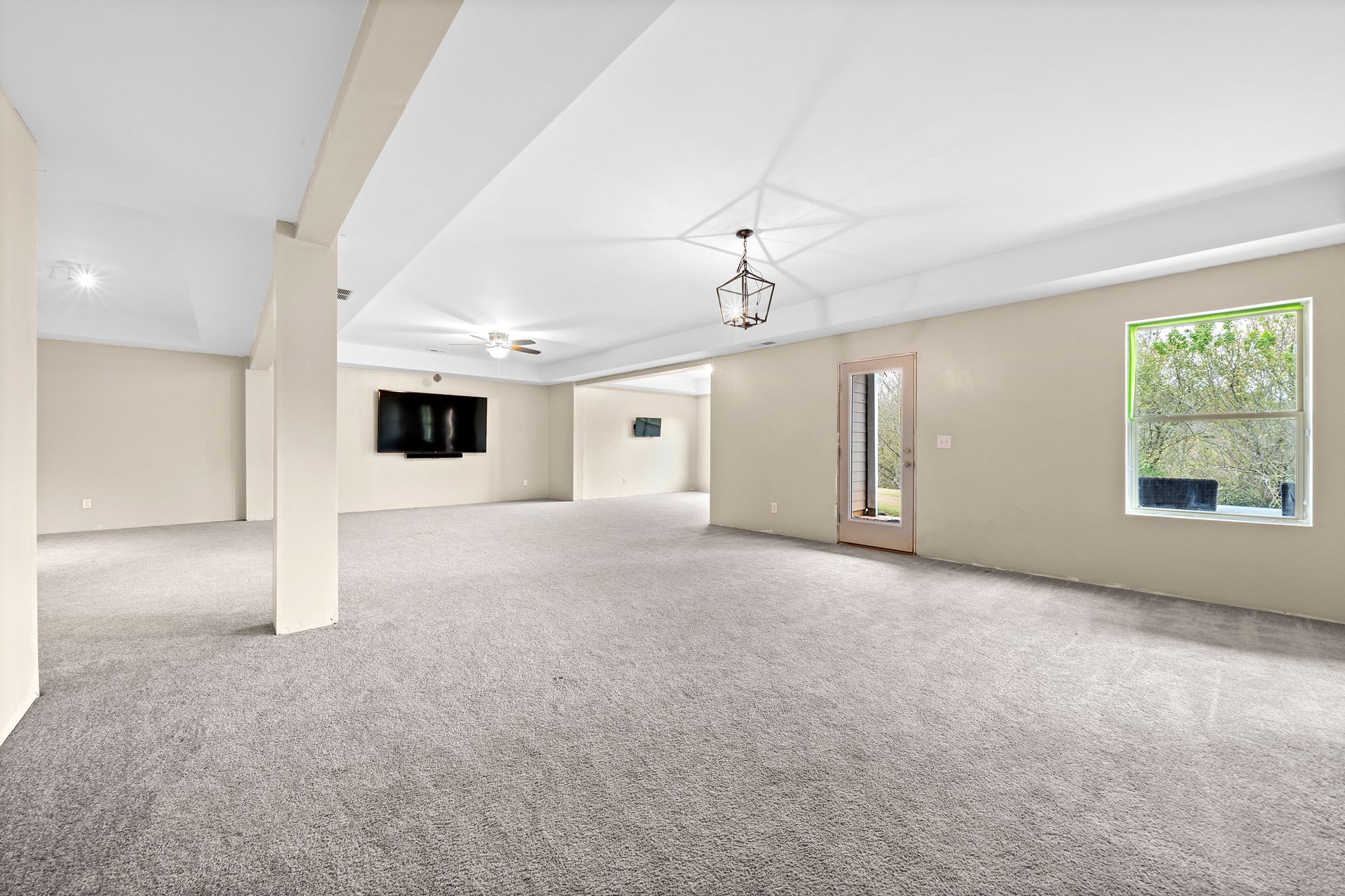 A large empty room with a carpeted floor and a television on the wall.