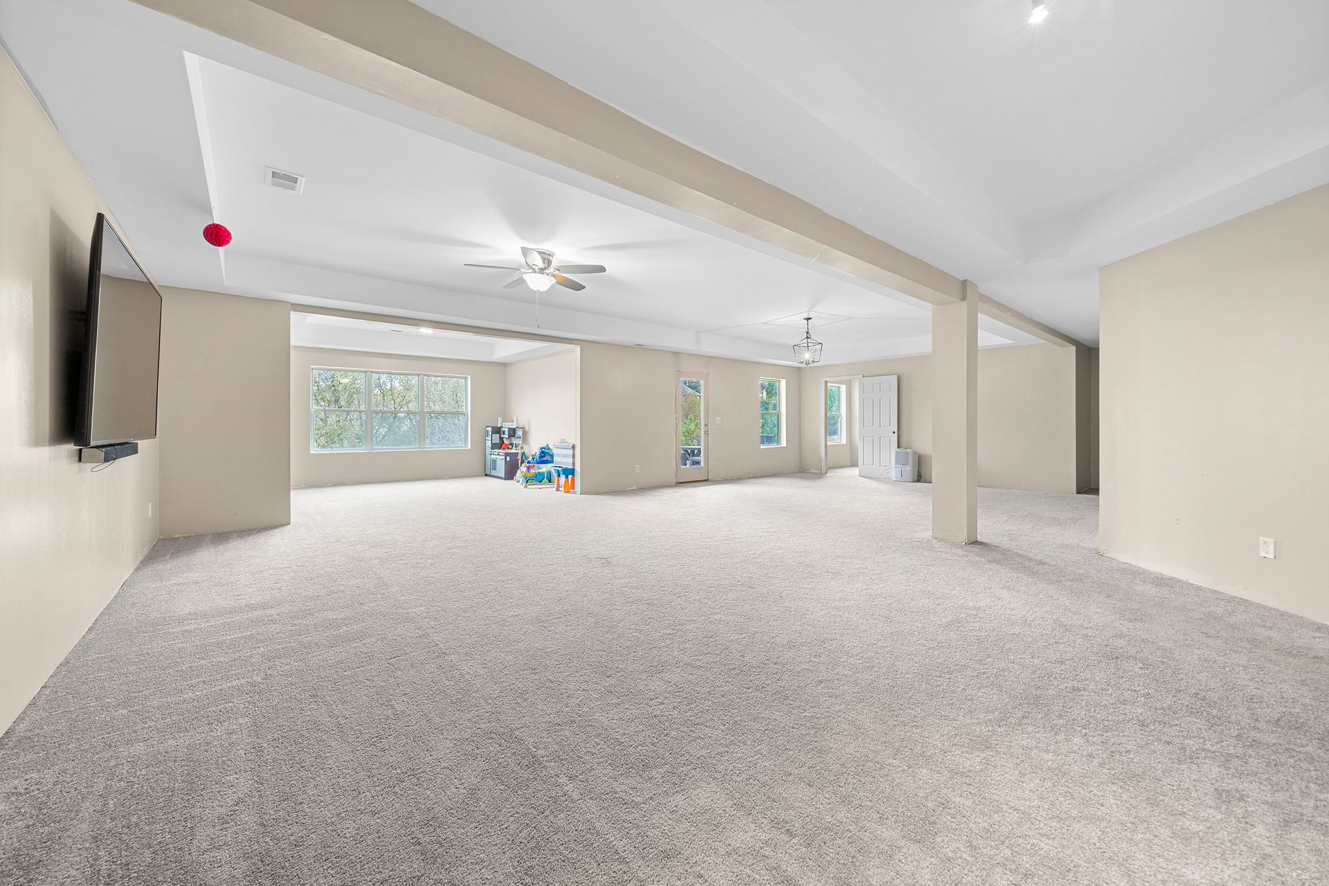 A large empty room with a carpeted floor and a flat screen tv mounted on the wall.