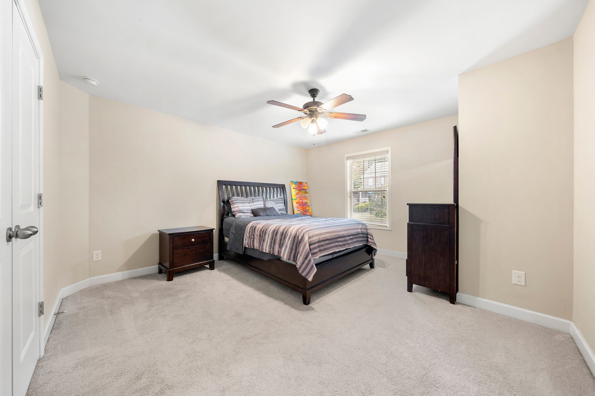 A bedroom with a bed , nightstand , dresser and ceiling fan.