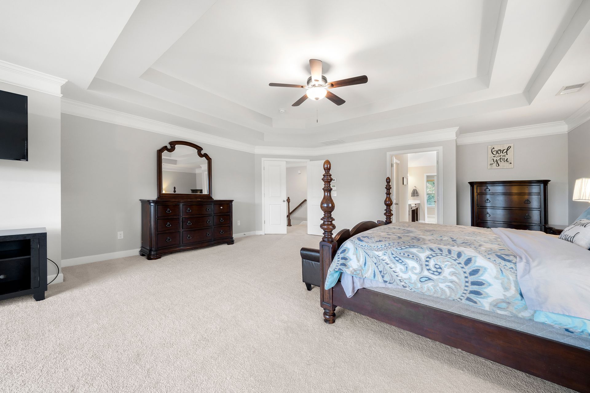 A bedroom with a large bed , dresser , mirror and ceiling fan.