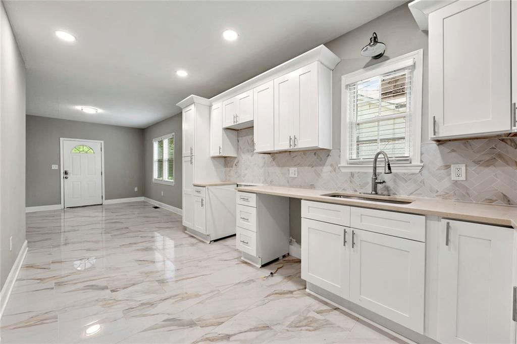 Modern white kitchen with marble-look countertops and flooring, connecting to a living area with a white door.