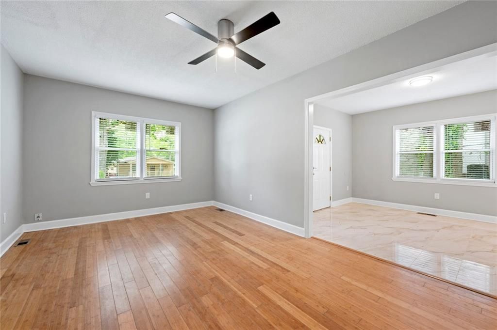 Empty room with hardwood floors, gray walls, ceiling fan, and windows.