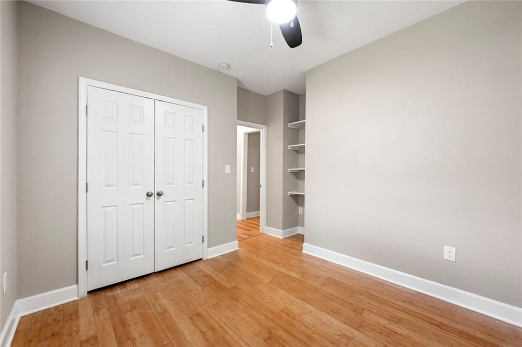 Empty bedroom with hardwood floors, white closet doors, gray walls, and built-in shelves.