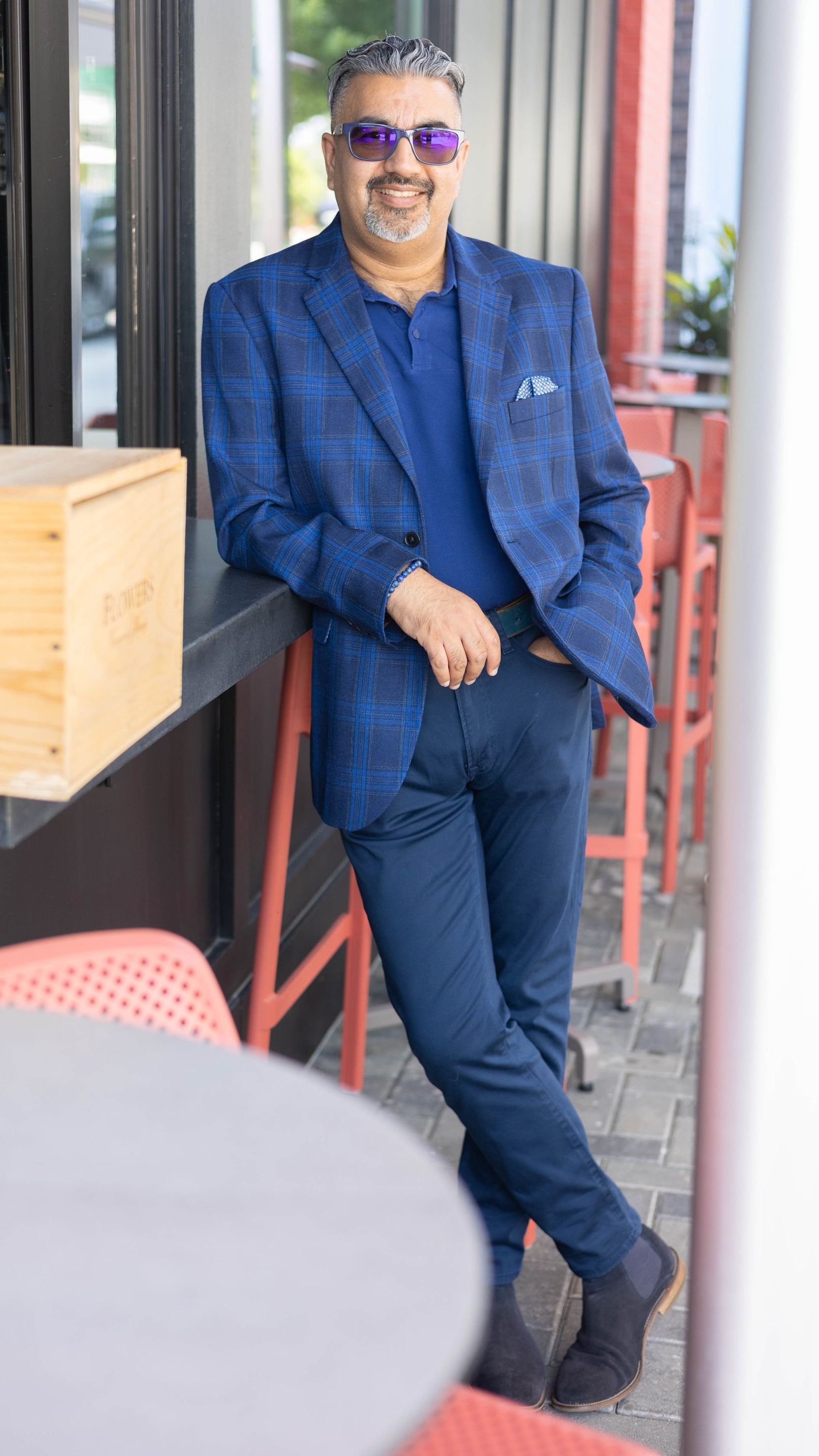 A man in a blue suit and sunglasses is standing next to a table.