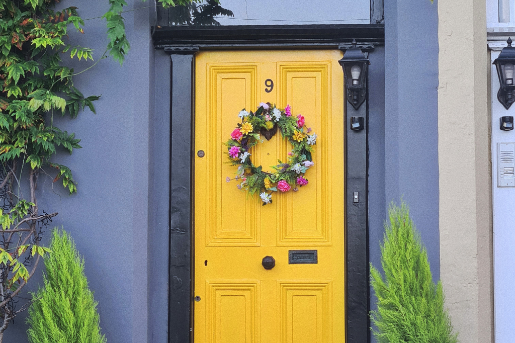 Yellow front door with wreath and number 9. Blue walls, black trim, and greenery.