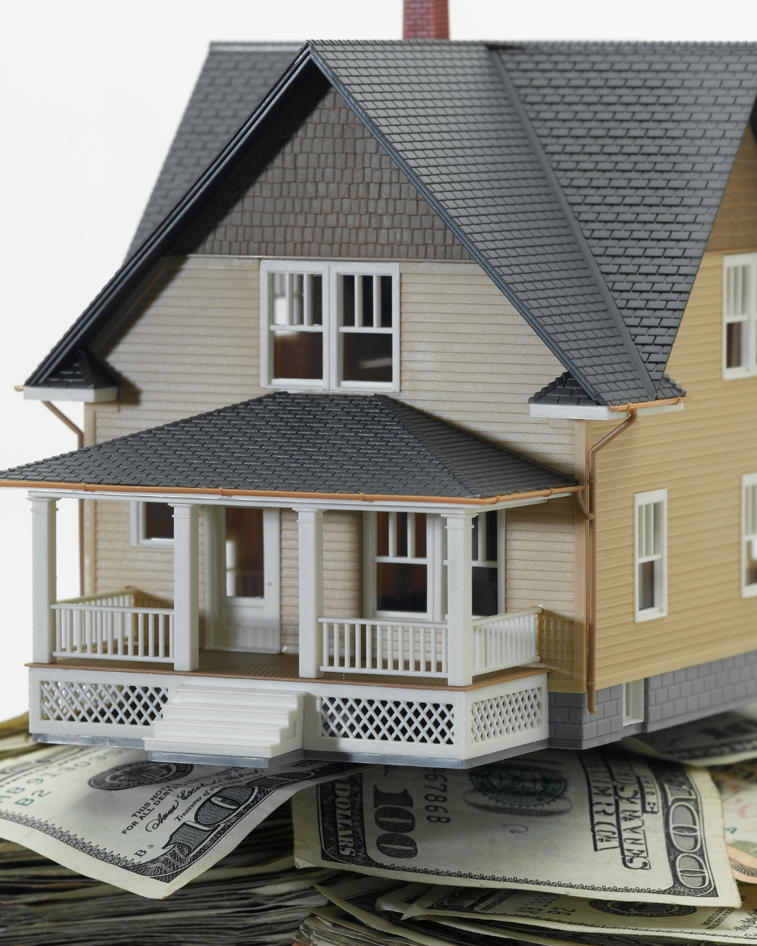 House model perched on a pile of hundred-dollar bills, symbolizing real estate investment.