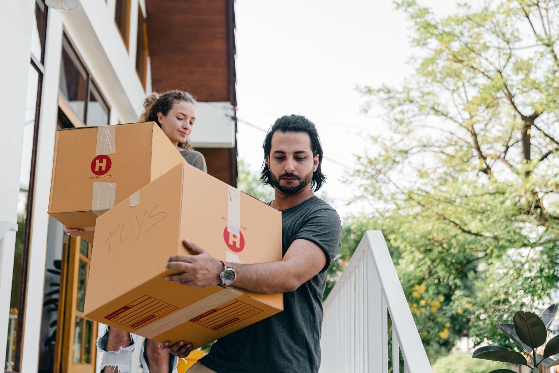 Two people carrying cardboard boxes up steps outside a house