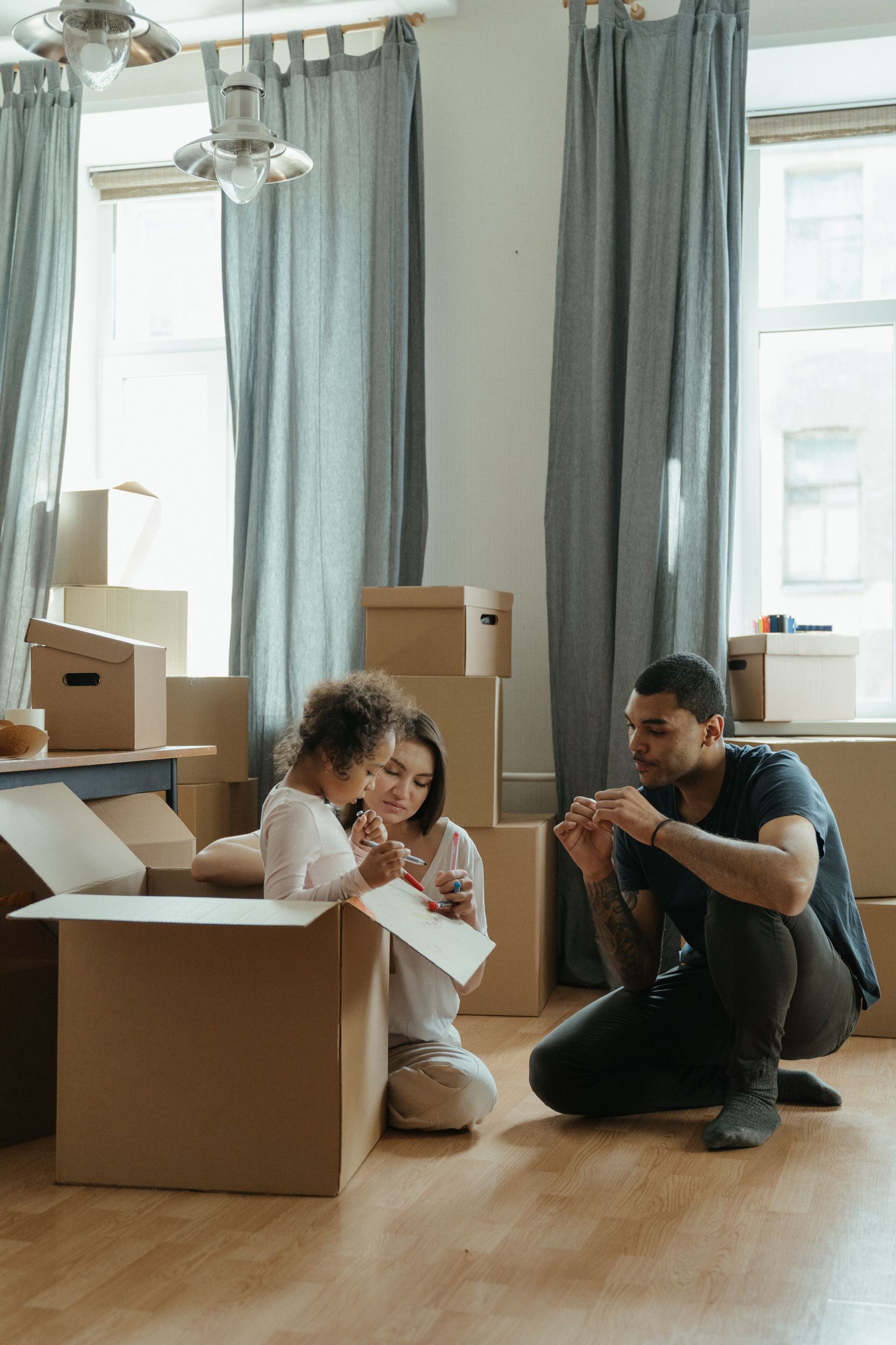 Two people sitting on a floor among moving boxes in a bright room, sorting items during a move