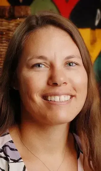 A woman with long hair is smiling and wearing a necklace.