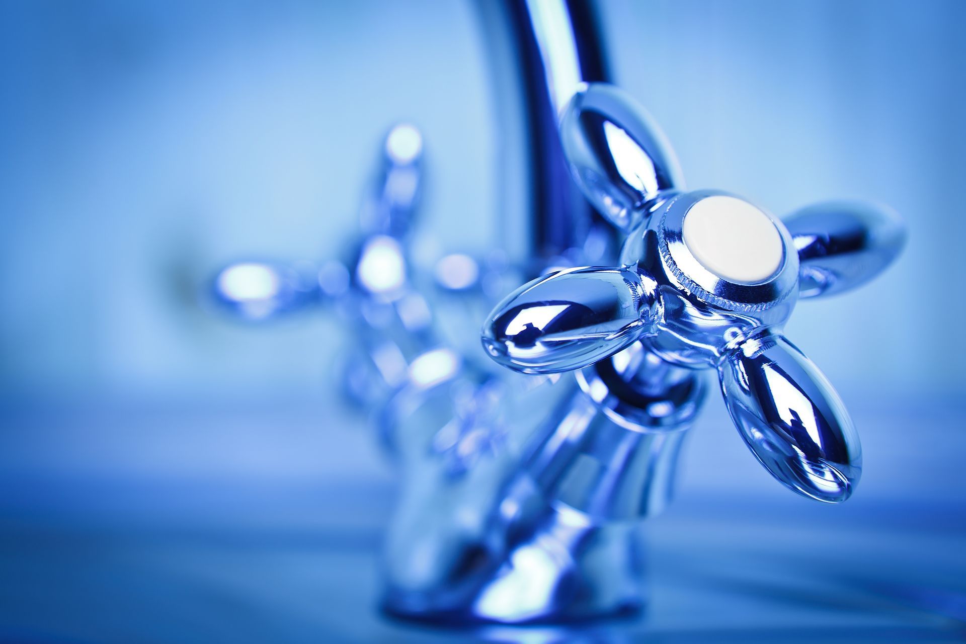 Close-up of a chrome faucet with water droplets against a soft blue background
