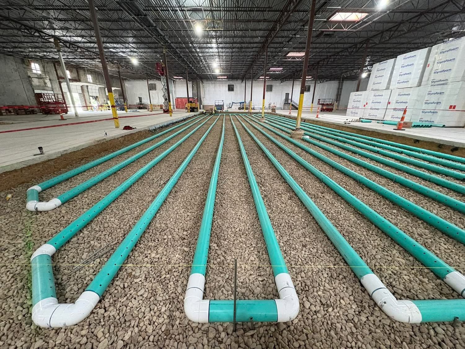Rows of turquoise pipes laid across a warehouse floor under construction.