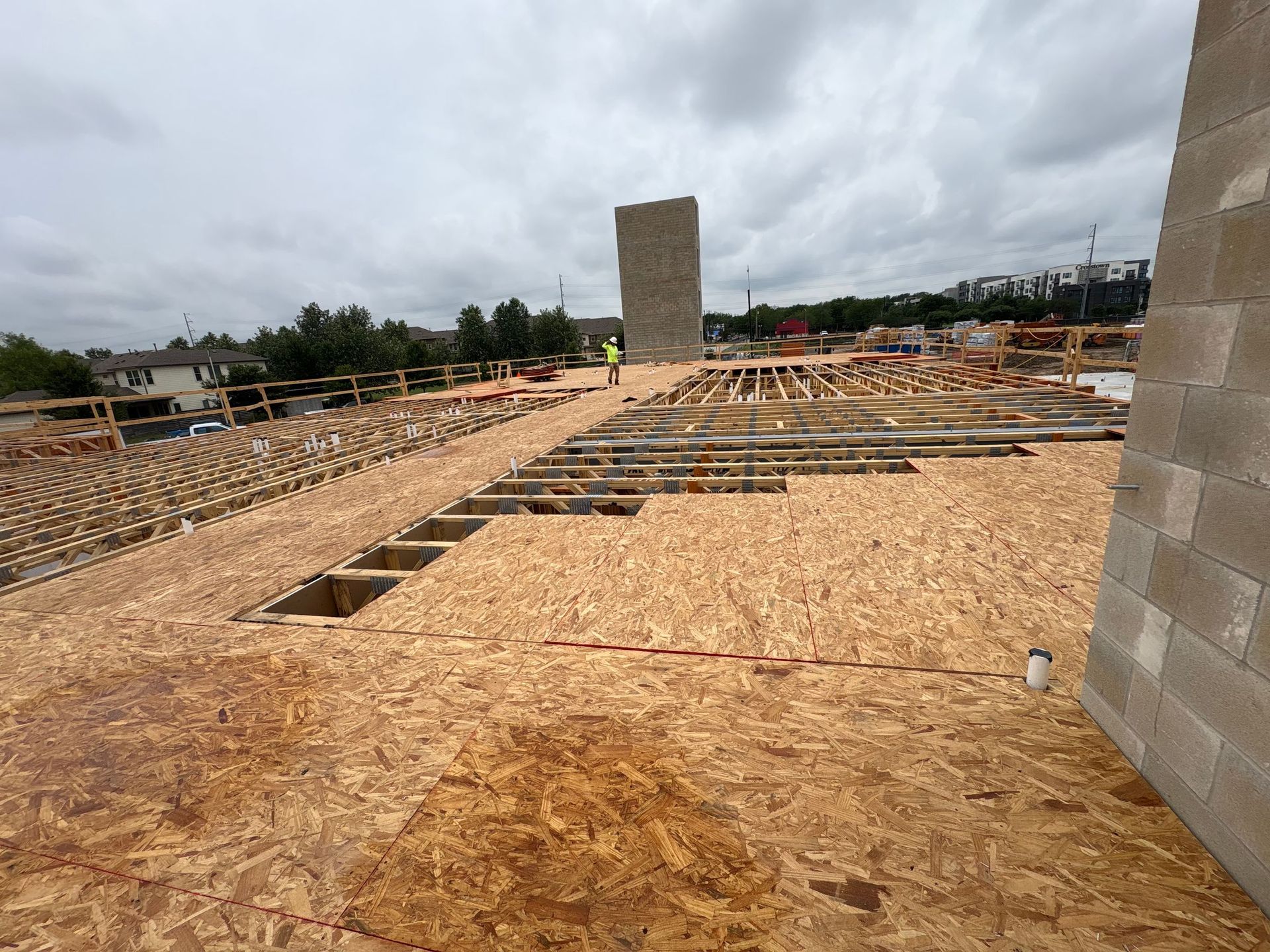 Construction site with plywood subfloor framing and a tall concrete wall under a cloudy sky