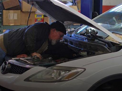 Mechanic inspecting a white car with hood open in a garage | Alexander’s Automotive, Inc.