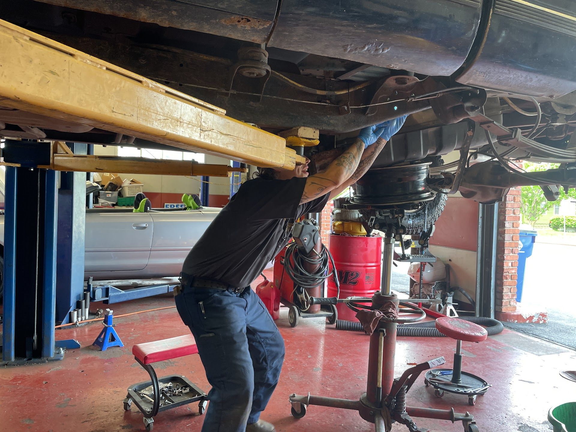 Mechanic under a lifted vehicle in a garage, working beneath the chassis with tools nearby | Alexander’s Automotive, Inc.
