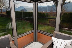 View from inside a gazebo with large windows overlooking a grassy yard and mountains.