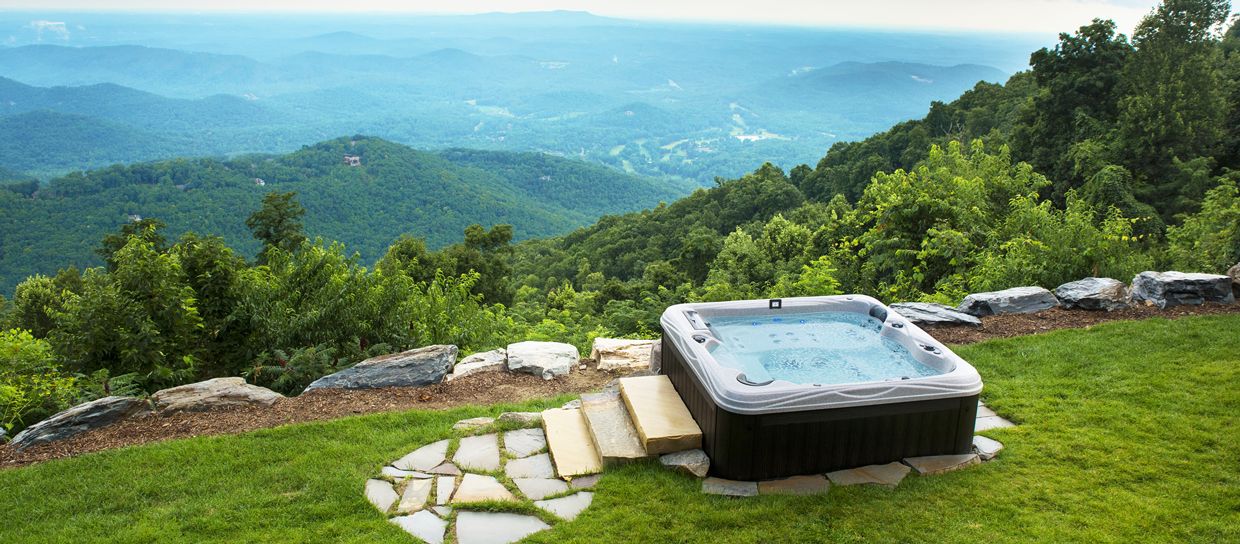 Hot tub on a grassy hillside overlooking a mountain range.