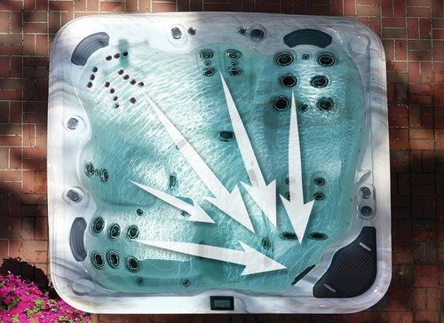 Overhead view of a hot tub with arrows indicating water jets. Turquoise water, gray interior, set on brick patio.