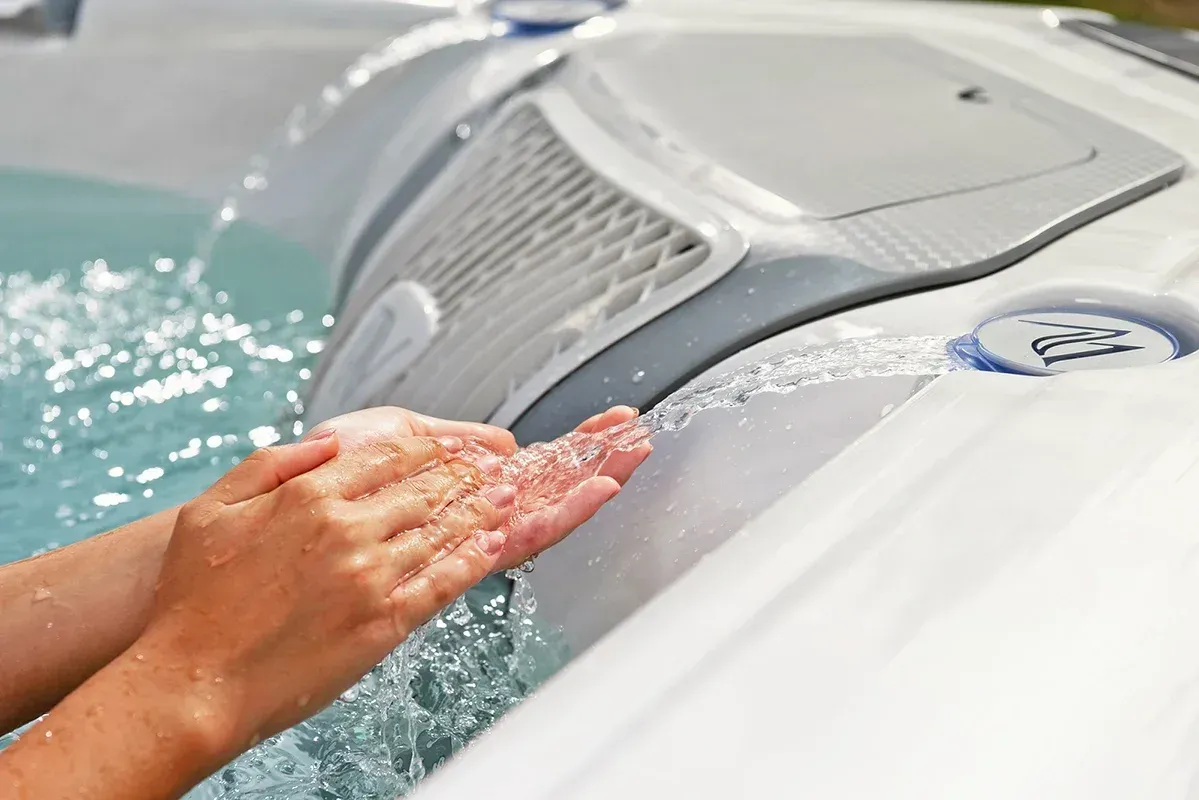 Person's hands catching water flowing from a hot tub's jets; close-up view.