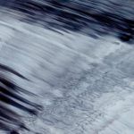 Abstract view of dark water and light reflections, creating blurred, wavy lines.