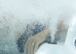 Hand with ring submerged in bubbly water, near a hot tub jet.