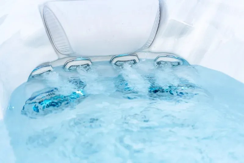 Close-up of a hot tub interior with jets of water spraying, illuminated in blue, white backdrop.