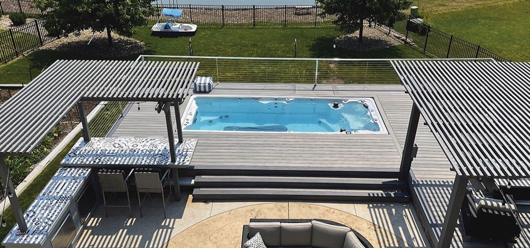An outdoor deck with a pool, pergola, and seating area overlooking a lake.