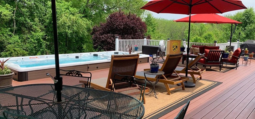 A deck with a pool, lounge chairs, red umbrellas, surrounded by greenery.