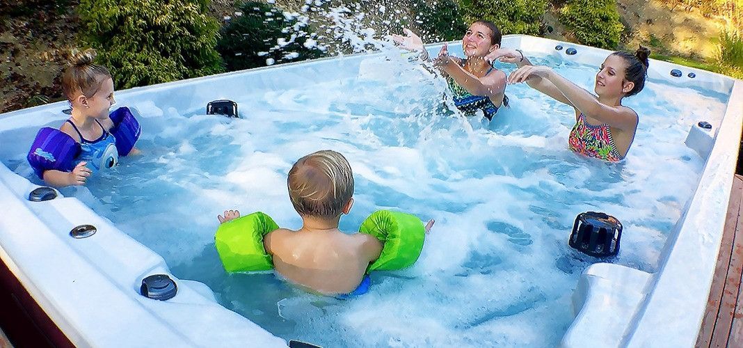 People splashing in a hot tub outdoors, with two children wearing arm floaties.
