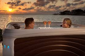 Couple relaxing in a hot tub, ocean view at sunset. Drinks on the edge.
