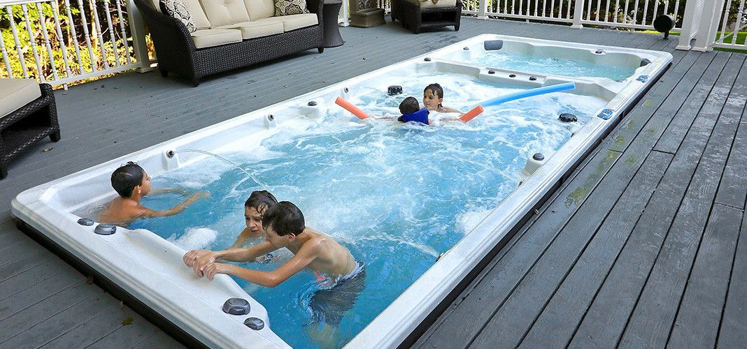 Children play in a rectangular pool on a wooden deck. Several children are in the pool, with others nearby.