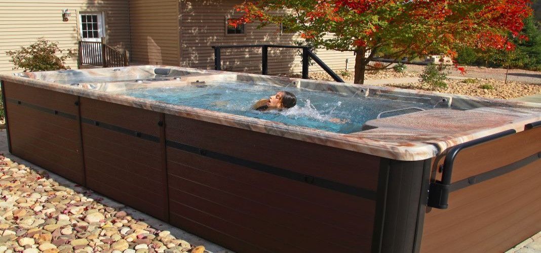 A person swimming in a long, narrow pool. Brown panels form the pool's sides, and colorful fall foliage is in the background.