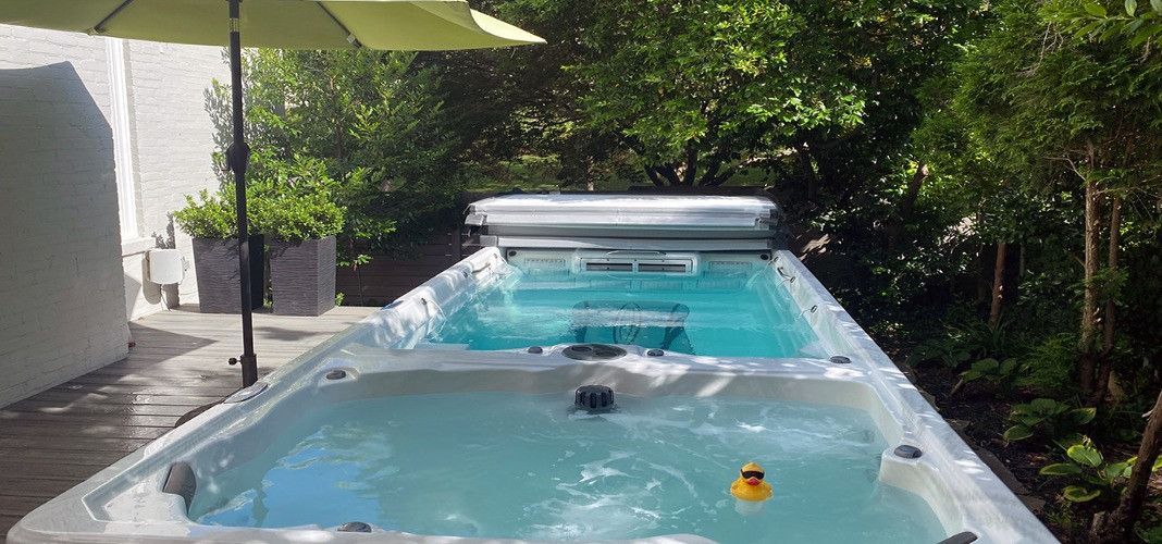 A long outdoor hot tub filled with water, a yellow rubber duck, and a green umbrella.