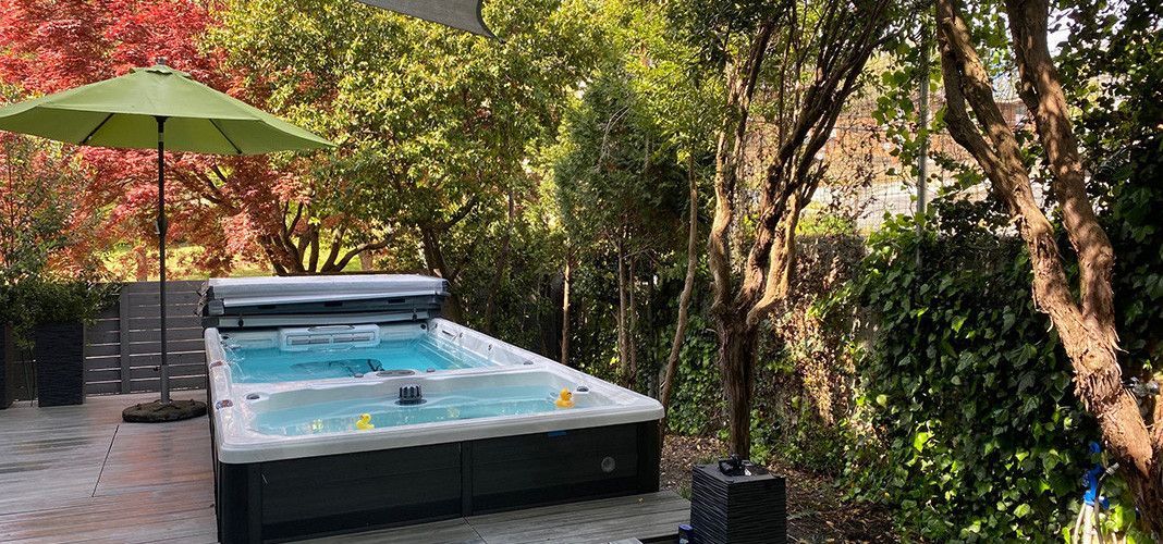 Outdoor swimming pool with an open cover and umbrella surrounded by trees.